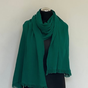 May include: A dark green, fringed scarf made of a soft, textured fabric. The scarf is draped over a black mannequin.