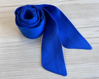 May include: A bright blue fabric sash or ribbon, rolled up and tied in a bow. The sash is made of a soft, textured fabric.