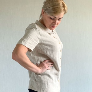 May include: A beige linen shirt with a collar and short sleeves. The shirt has a button-up front and is made of a lightweight fabric.