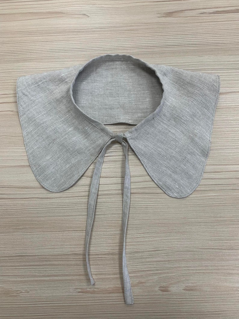 May include: A grey linen collar with a tie fastening. The collar is large and has a rounded shape.