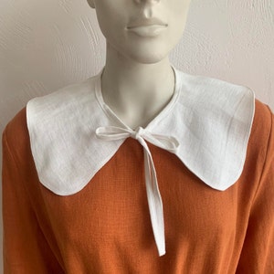 May include: A white linen collar with a bow tie, worn over a rust-coloured dress.
