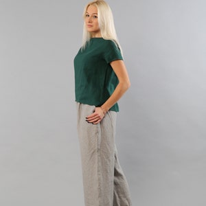 May include: A woman wearing a green linen top and gray linen pants. She is standing on a gray background.