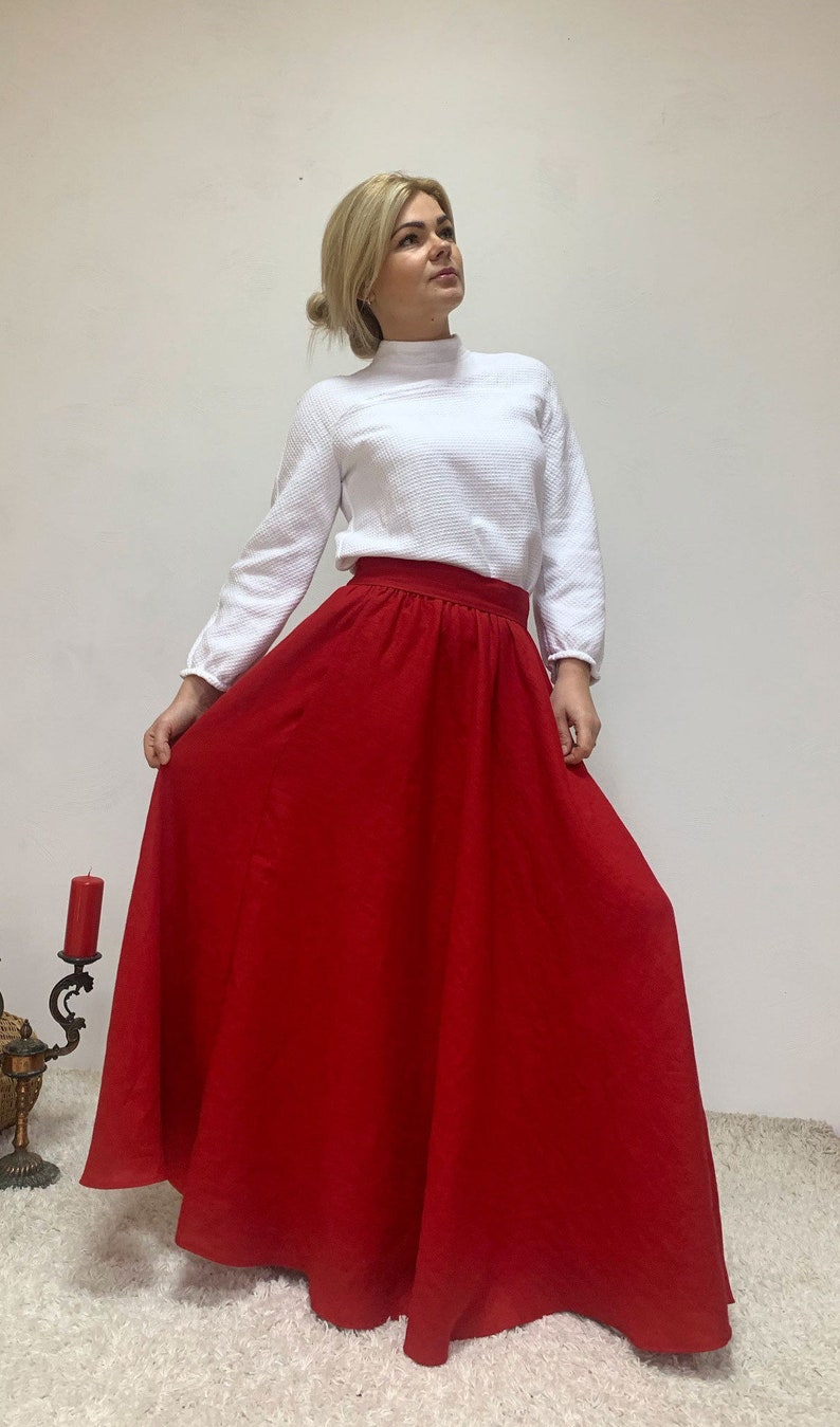 May include: A red maxi skirt with a high waist and a flowy silhouette. The skirt is made of a lightweight fabric and has a simple design.