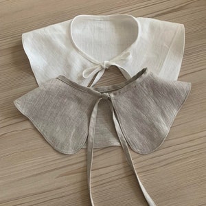 May include: Two fabric collars, one white and one beige, with a tied bow at the back.