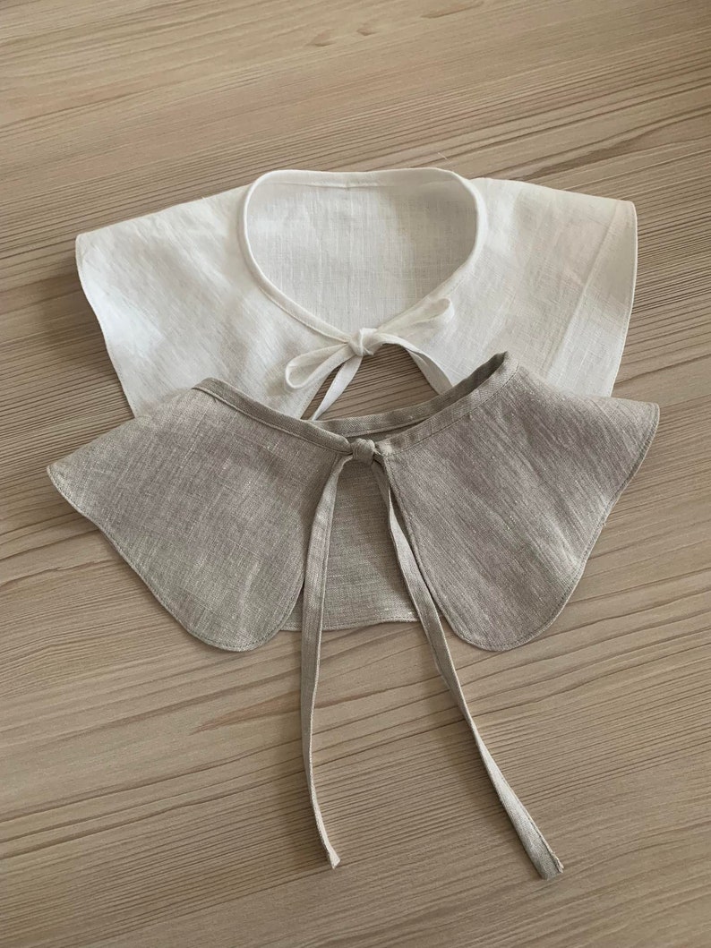 May include: Two fabric collars, one white and one beige, with a tied bow at the back.