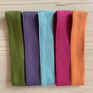 May include: Five fabric strips in different colors: olive green, purple, light blue, burgundy, and orange. The strips are all the same size and are arranged horizontally.
