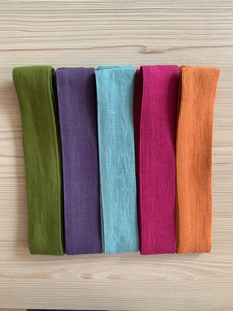 May include: Five fabric strips in different colors: olive green, purple, light blue, burgundy, and orange. The strips are all the same size and are arranged horizontally.