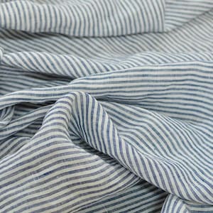 Peut inclure: Gros plan sur un tissu blanc à fines rayures bleues. Le tissu est froissé et plié, montrant la texture du matériau.