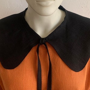 May include: A black linen collar with a tie fastening, worn over an orange linen shirt.
