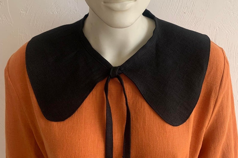 May include: A black linen collar with a tie fastening, worn over an orange linen shirt.
