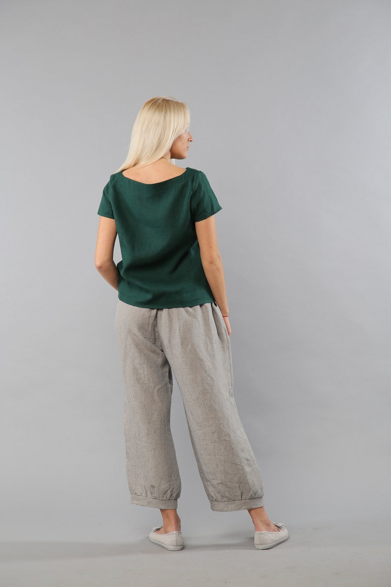 May include: A woman wearing a dark green linen top and gray linen pants. The pants have a wide leg and a cuffed hem.