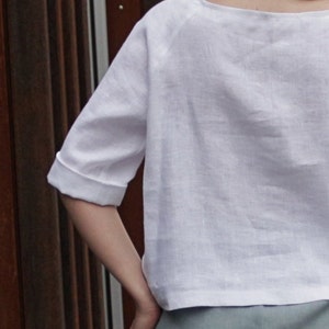 May include: A white linen top with a scoop neck and three-quarter sleeves. The top is loose-fitting and has a relaxed silhouette.