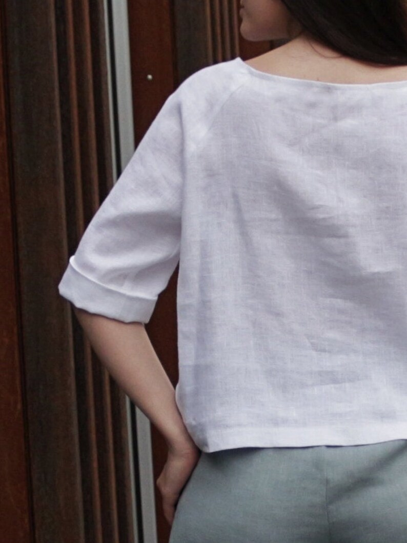 May include: A white linen top with a scoop neck and three-quarter sleeves. The top is loose-fitting and has a relaxed silhouette.