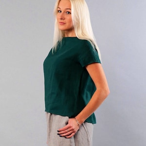 May include: A woman wearing a dark green linen top with short sleeves and a light gray linen skirt.