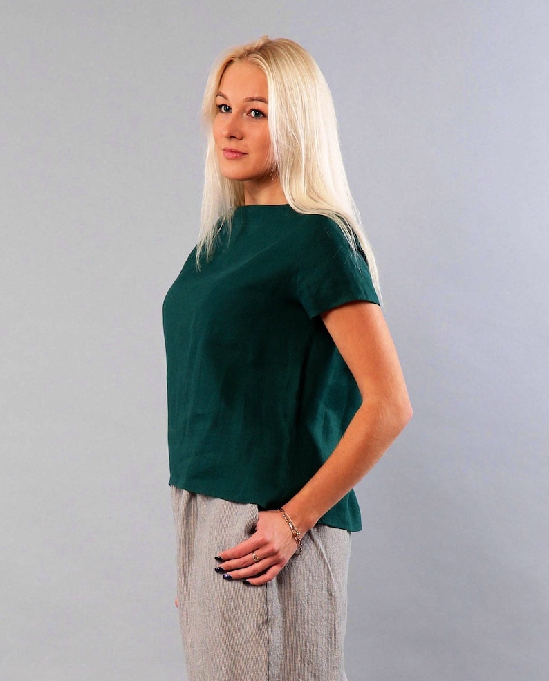 May include: A woman wearing a dark green linen top with short sleeves and a light gray linen skirt.