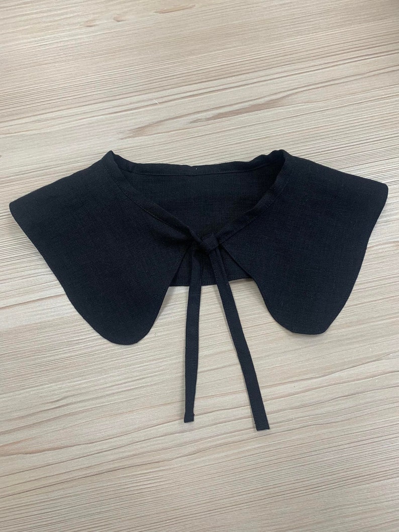 May include: A black fabric collar with a tie at the back. The collar is designed to be worn over a shirt or blouse.
