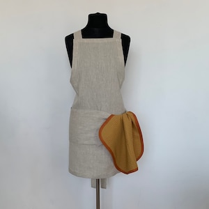 May include: A beige linen apron with adjustable straps and a brown waffle weave kitchen towel tied around the waist.