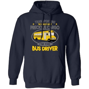 Puede incluir: Sudadera con capucha azul marino con un autobús escolar amarillo. El texto dice: "Transportando la carga más preciada del mundo. Soy el conductor del autobús."