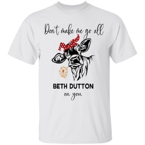 May include: White t-shirt with a black and white illustration of a cow wearing a red bandana. The text "Don't make me go all Beth Dutton on you" is printed on the shirt.