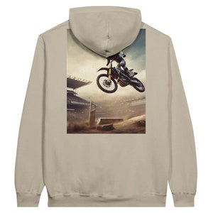 May include: Beige hoodie featuring a motocross scene on the back. The graphic depicts a dirt bike rider mid-air over a jump in a stadium. The hoodie is a neutral color, suitable for casual wear.
