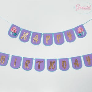 Puede incluir: Pancarta de fieltro morado con letras doradas brillantes que deletrean "Happy Birthday" con ilustraciones de sirenas en cada extremo.