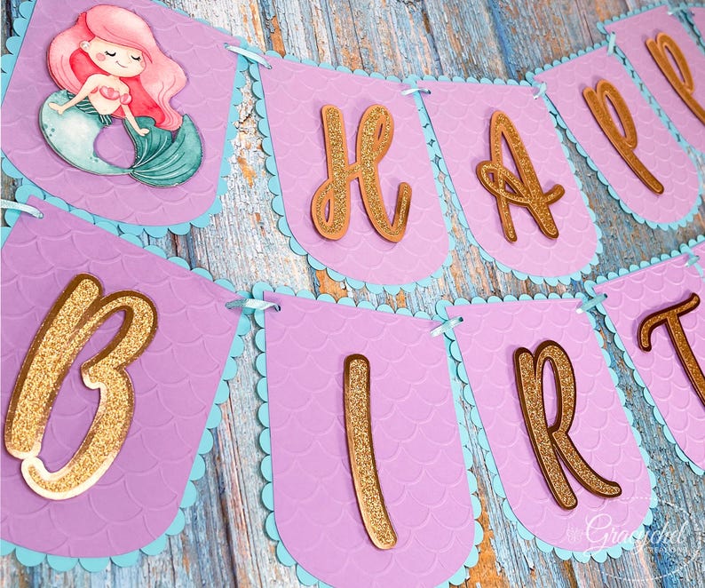 Puede incluir: Bandera morada y azul con letras doradas de purpurina que deletrean "Happy Birthday". La bandera tiene un dise&ntilde;o de sirena con una ilustraci&oacute;n de sirena en la primera bandera.