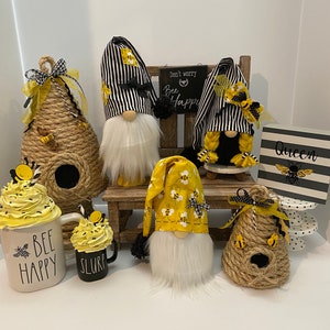 May include: A collection of bee-themed home decor items, including gnomes, beehives, mugs, and a sign that reads "Don't worry, bee happy".