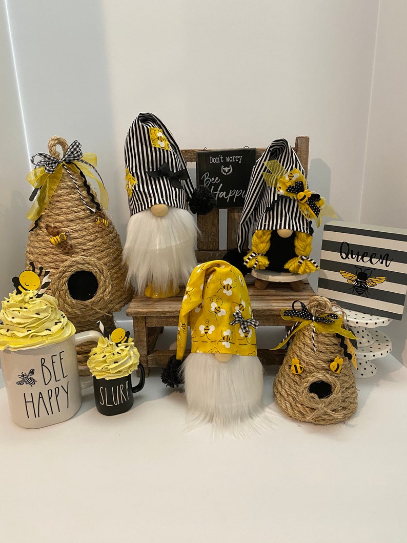 May include: A collection of bee-themed home decor items, including gnomes, beehives, mugs, and a sign that reads "Don't worry, bee happy".