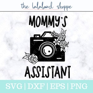 May include: Black and white graphic design of a camera with flowers and the text "Mommy's Assistant". The text "SVG | DXF | EPS | PNG" is below the graphic.