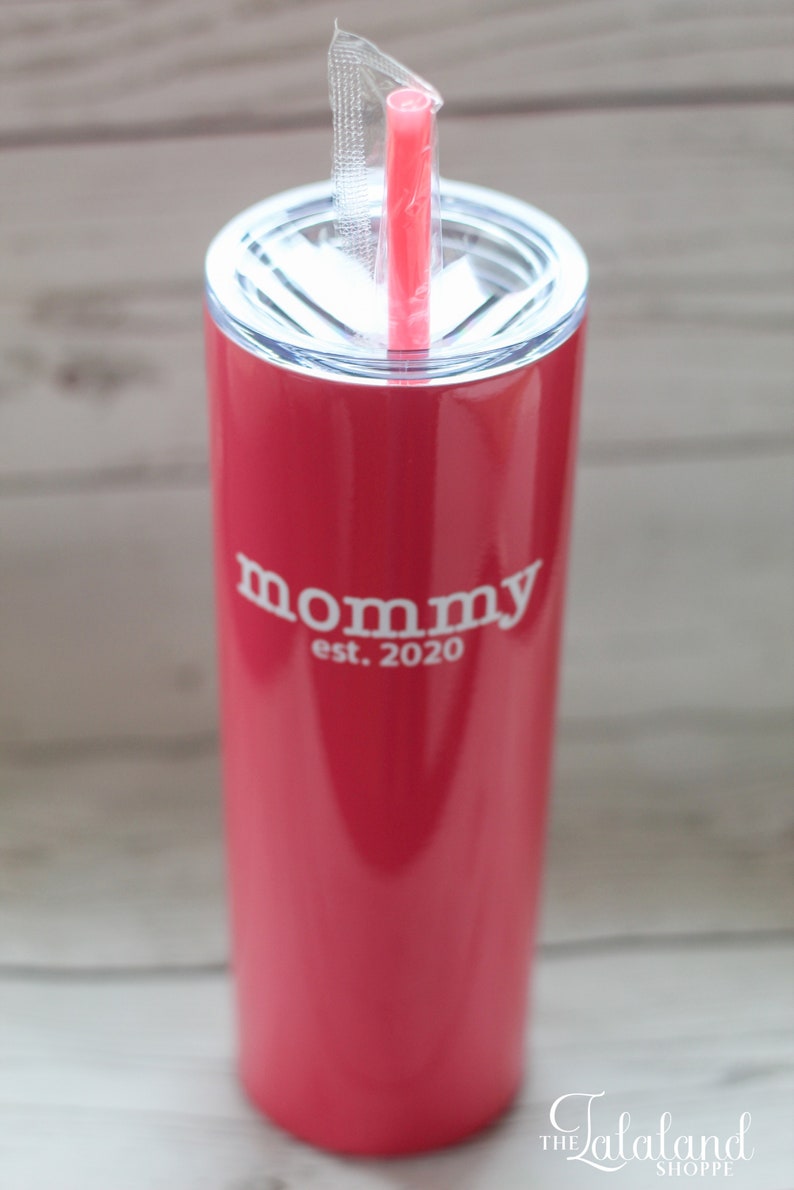 Puede incluir: Un vaso de acero inoxidable rosa con tapa blanca y una pajita blanca. El vaso tiene el texto "mommy est. 2020" impreso en el lateral.