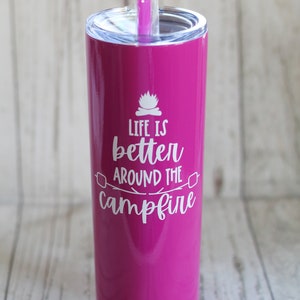 May include: A pink stainless steel tumbler with a white lid and a white straw. The tumbler has the text "Life is better around the campfire" printed on it.