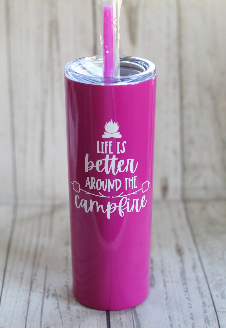 May include: A pink stainless steel tumbler with a white lid and a white straw. The tumbler has the text "Life is better around the campfire" printed on it.