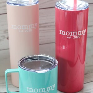 Puede incluir: Tres vasos de acero inoxidable con una inscripci&oacute;n blanca que dice "mommy est. 2020". Los vasos son de color rosa, rojo y turquesa.