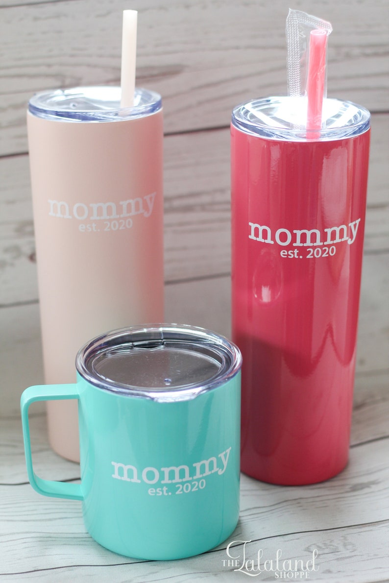 Puede incluir: Tres vasos de acero inoxidable con una inscripci&oacute;n blanca que dice "mommy est. 2020". Los vasos son de color rosa, rojo y turquesa.