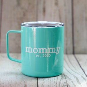 Puede incluir: Una taza de viaje de acero inoxidable azul turquesa con una tapa blanca y una inscripci&oacute;n blanca que dice "mommy est. 2020".