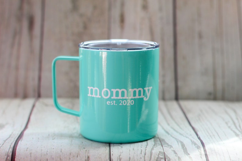 Puede incluir: Una taza de viaje de acero inoxidable azul turquesa con una tapa blanca y una inscripci&oacute;n blanca que dice "mommy est. 2020".