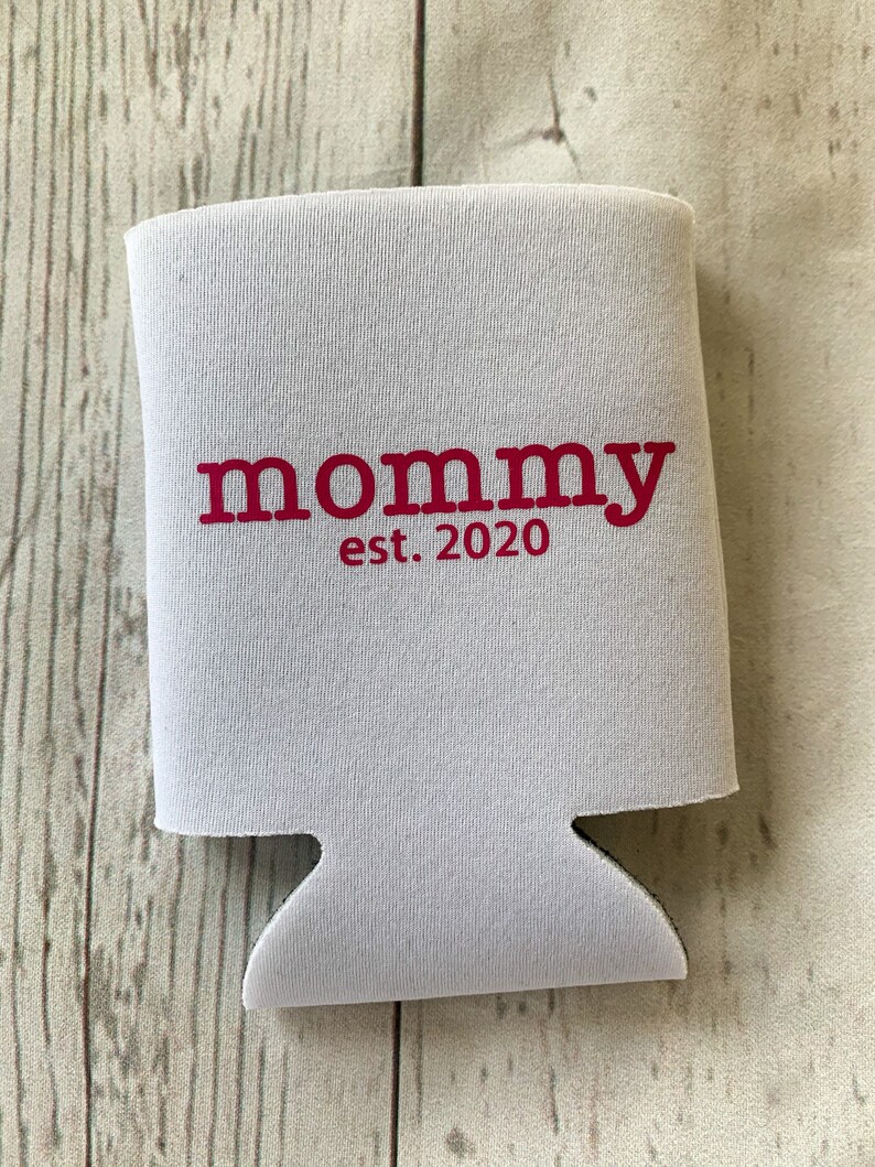 Puede incluir: Enfriador de latas de espuma blanca con el texto "mommy est. 2020" en rojo.