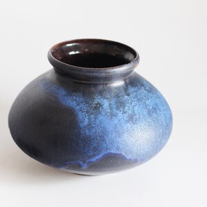 Könnte beinhalten: Eine dunkelblaue und schwarze Keramikvase mit einem marmorierten Überzug. Die Vase hat einen runden Körper und eine breite Öffnung.