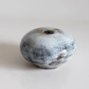 Może przedstawiać: Mały, okrągły, biały ceramiczny wazon z czarnymi plamkami. Wazon ma mały otwór na górze.