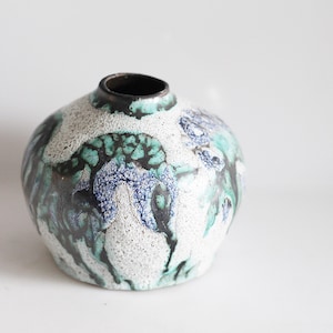 Może przedstawiać: Biały ceramiczny wazon z abstrakcyjnym wzorem w kolorze niebieskim, zielonym i czarnym. Wazon ma okrągły korpus i wąski otwór.