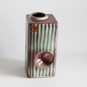 May include: A brown and green striped ceramic vase with a hole in the side. The vase has a square shape and a textured surface.