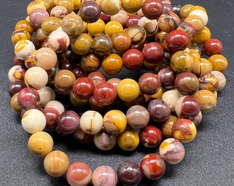 Puede incluir: Una colección de cuentas redondas y pulidas en varios colores, incluyendo tonos de amarillo, rojo, marrón y crema. Las cuentas están ensartadas, formando una pulsera o collar. Las cuentas tienen un acabado liso y brillante.