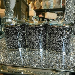 May include: Three matching tea, coffee, and sugar canisters. Each has a black, glitter-covered body and a silver rim. The lids are adorned with a clear, faceted crystal. The words "Tea", "Coffee", and "Sugar" are etched on the front of each canister.