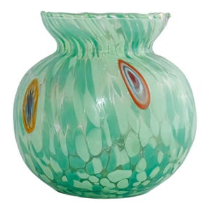May include: A round, light green glass vase with a wide body and a narrow, ruffled neck. The vase features colourful, oval-shaped accents in orange, red, and blue. The glass has a speckled pattern throughout.