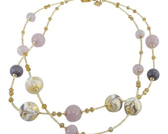 May include: A layered necklace featuring a delicate gold chain adorned with various beads. The necklace includes round, smooth beads in shades of lavender, gray, and cream with gold accents. Small, amber-colored beads are interspersed along the chain.