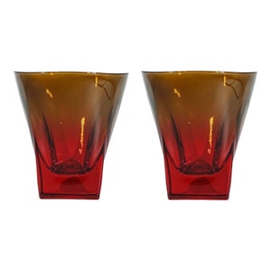 May include: Two clear glass tumblers with a red and brown ombre effect. The glasses are square shaped with a rounded bottom.