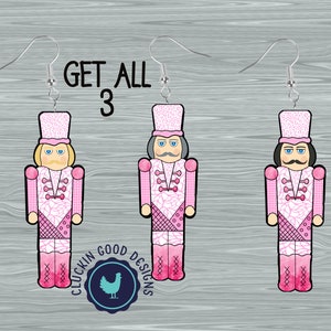 May include: Three pink and white nutcracker earrings with silver hooks. Each earring features a different nutcracker design with a pink hat and uniform. The text "GET ALL 3" is above the earrings.