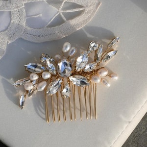 May include: Gold hair comb with clear crystal and pearl embellishments. The comb has a floral design with a cluster of crystals in the center.