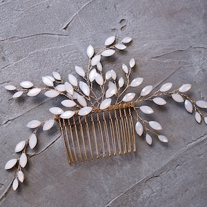 May include: A gold hair comb with white opal-like stones arranged in a leafy design. The comb is a bridal hair accessory.