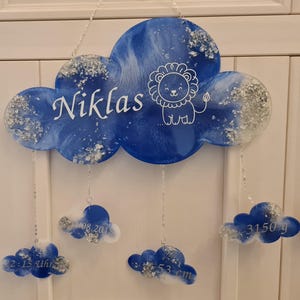 Könnte beinhalten: Blau-weißes, wolkenförmiges Baby-Namensschild aus Harz mit silbernem Glitzer. Das Schild trägt die Aufschrift "Niklas" und enthält eine Löwenillustration. Vier kleinere Wolken hängen an der Hauptwolke mit folgenden Details: "08.2018", "2:15 Uhr", "53 cm" und "3150 g".